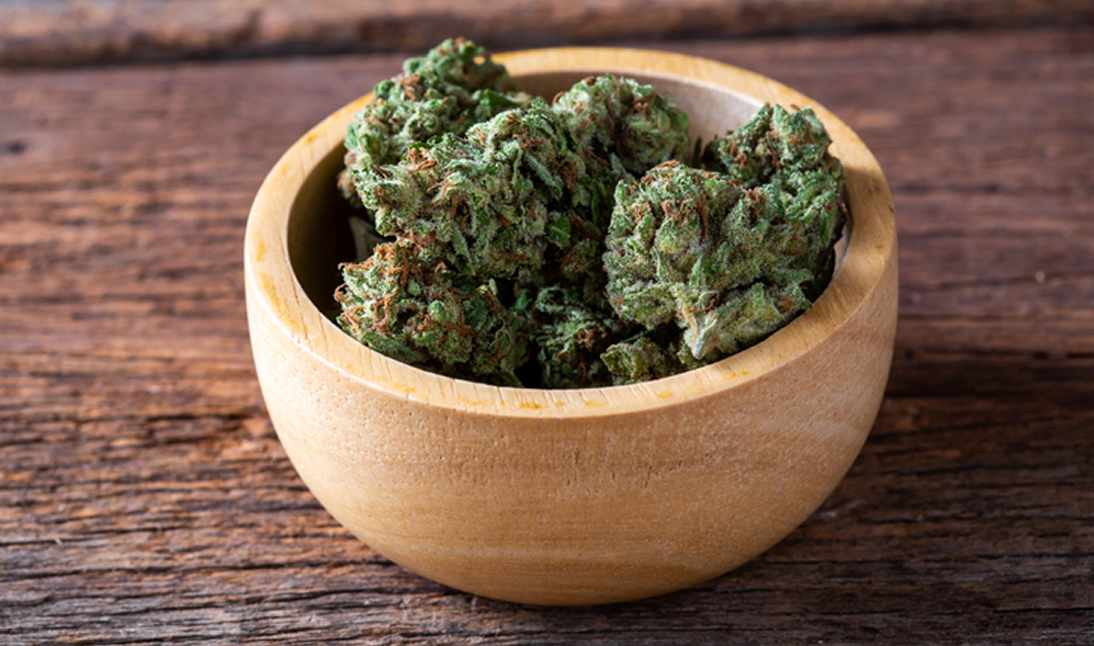 Wooden bowl with cannabis buds on table.