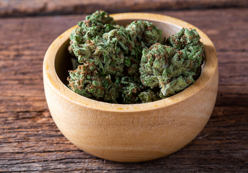 Wooden bowl with cannabis buds on table.
